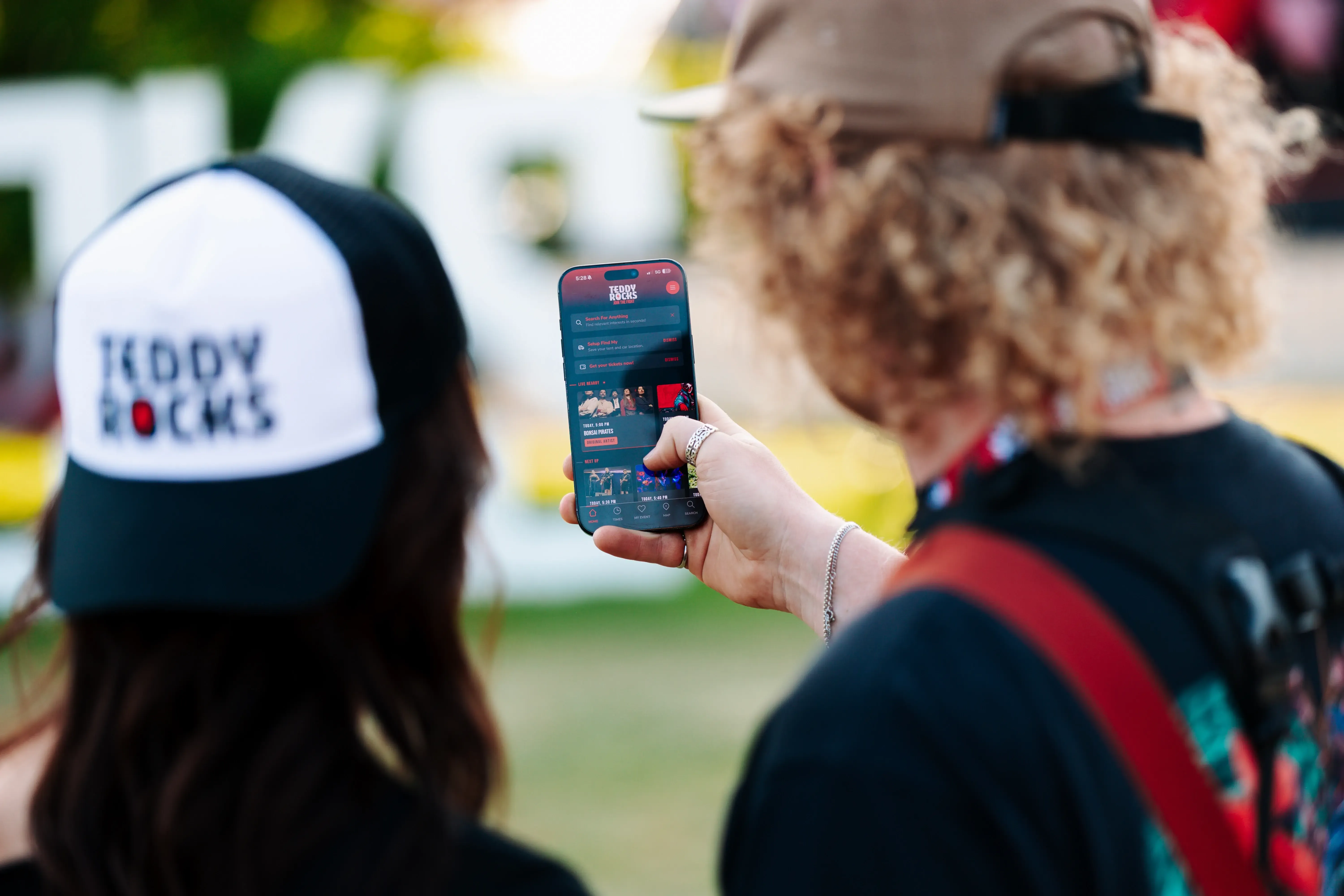 Two festival attendees using the Teddy Rocks event app on a phone outdoors